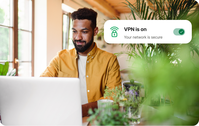 一名男子正對著筆電微笑，身邊有許多植栽